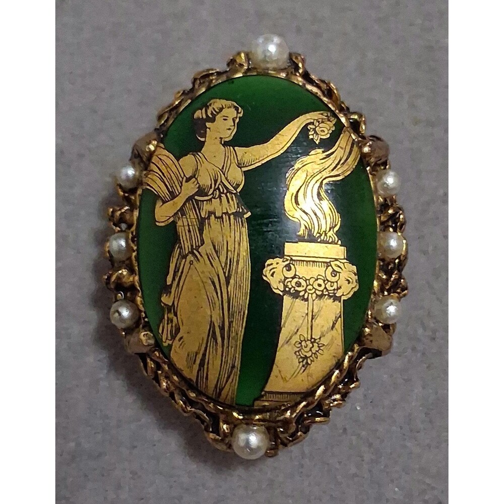 Green and gold oval pendant with figure of classical woman standing by a flame,